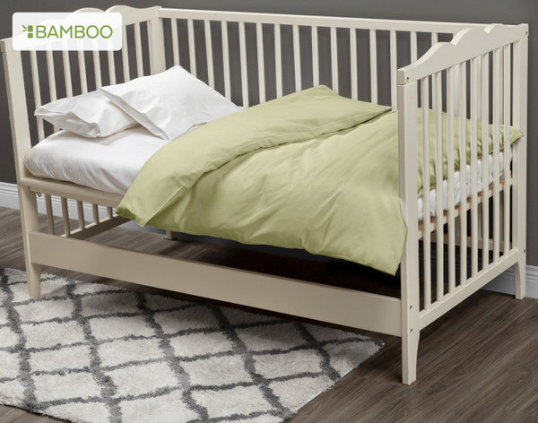 Our Bamboo Cotton Crib-Sized Duvet Cover in Elm Green dressed over a small white mattress in a cream white crib.