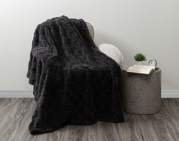 Angled view of our Checkered Teddy Throw in Charcoal draped over a modern grey armchair in a white room.