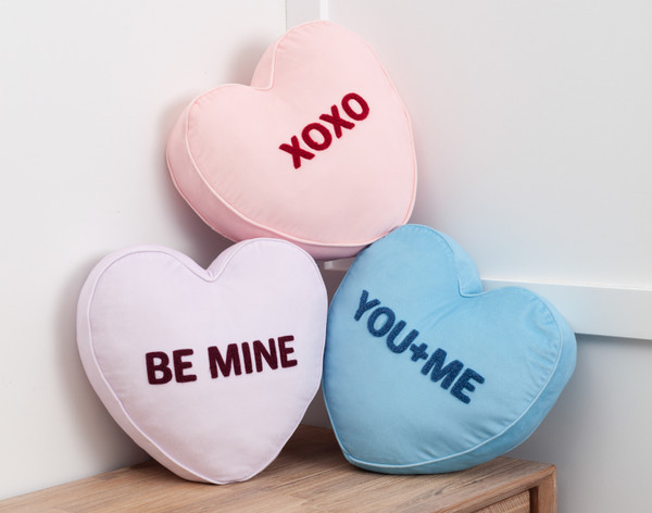 Our XOXO, Be Mine, and You & Me Candy Heart Cushions piled neatly in a bedroom corner on top of a dresser.