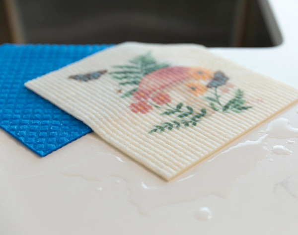 Angled view of our Mushroom Swedish Dishcloth Set absorbing water on a countertop.