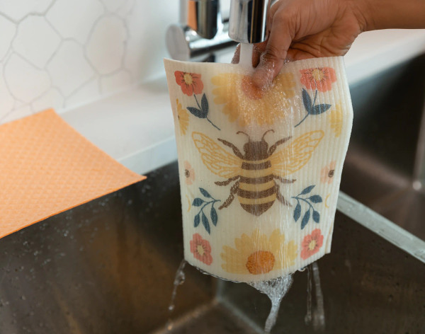 Side view of our Bee Swedish Dishcloth Set under a sink to be rinsed for reuse.