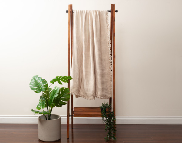 Front view of our Natural Muslin Gauze Blanket hanging from a fixture next to a small leafy plant.