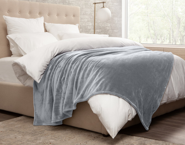 Side view of our Cashmere Touch Fleece Blanket in Slate Blue draped over a messy white bed.