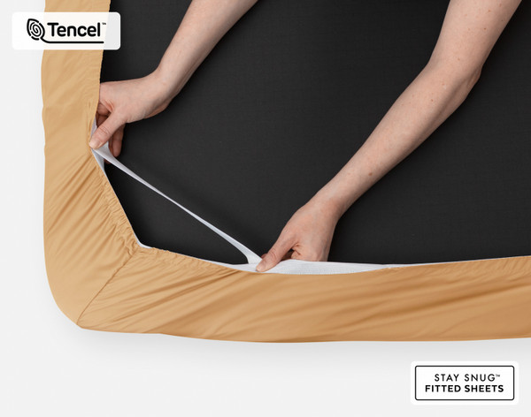 Bottom side of our BeechBliss TENCEL™ Modal Fitted Sheet in Gilded with two hands showing the Snug Fit elastics holding it tightly on the mattress.