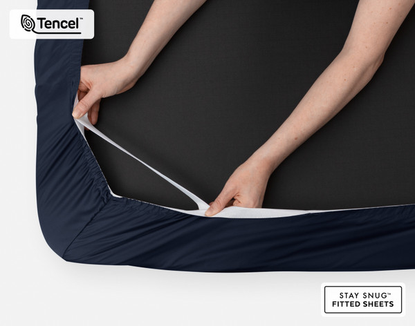Bottom side of our BeechBliss TENCEL™ Modal Fitted Sheet in Deep Space with two hands showing the Snug Fit elastics holding it tightly on the mattress.