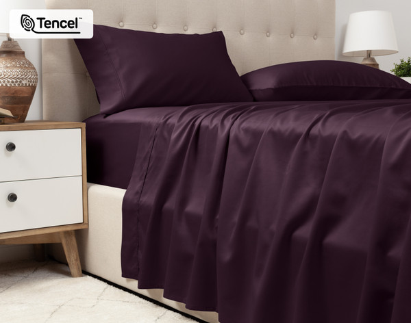 Lower view of our Eucalyptus Luxe TENCEL™ Lyocell Sheet Set in Purple to show its flat sheet draped over the side of a queen bed.