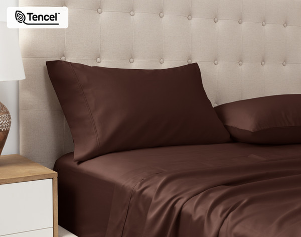 Angled view of our Eucalyptus Luxe TENCEL™ Lyocell Pillowcases in Chestnut sitting against a headboard of a beige queen bed.