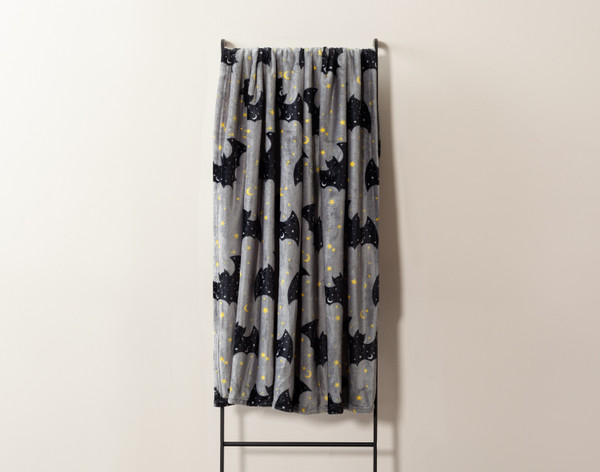 Front view of our Moonlit Bats Halloween Fleece Throw hanging on a tall rack against a solid grey wall.