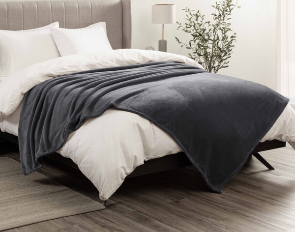 Side view of our Cashmere Touch Fleece Blanket in Graphite draped over a messy white bed.
