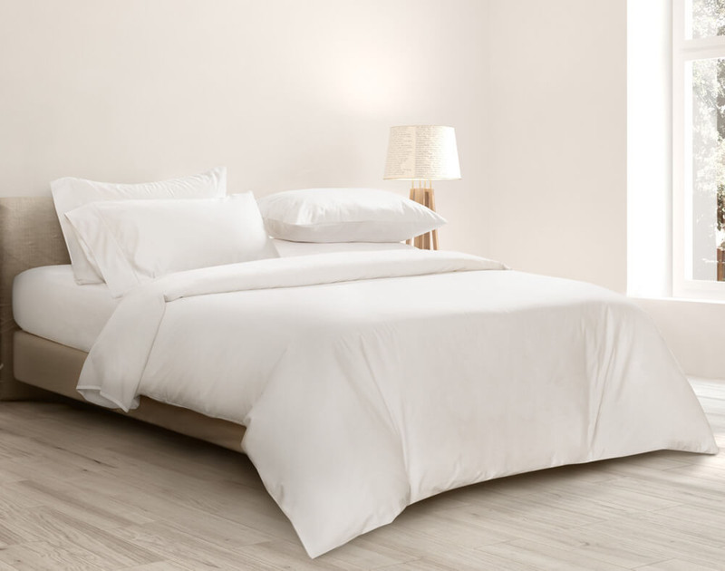 Angled view of our Bamboo Cotton Duvet Cover in White draped over a queen bed in a white bedroom.