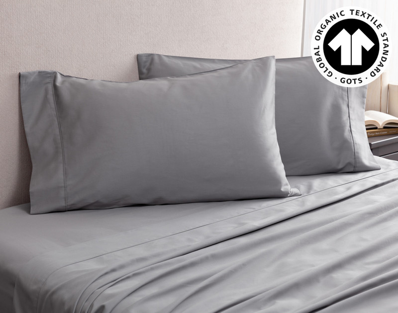 Angled view of our Organic Cotton Pillowcases in Sleet resting on an empty bed with matching sheets.