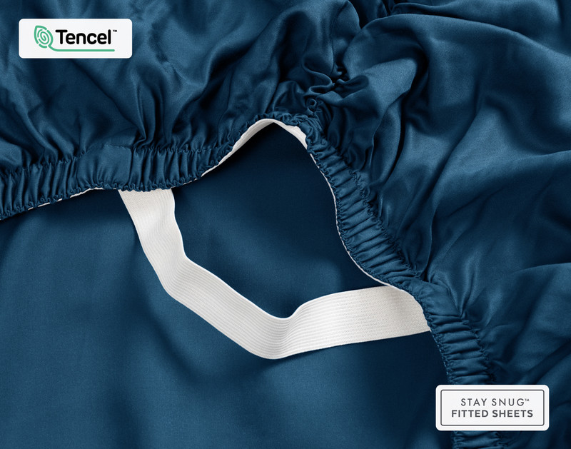 Face inférieure de notre BeechBliss TENCEL™ Modal Fitted drap en Seaport Blue avec deux mains montrant les élastiques Snug Fit qui le maintiennent fermement sur le matelas.