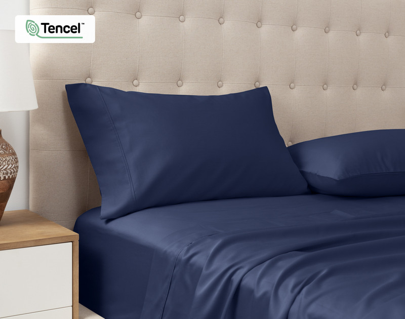 Vue en angle de nos Taies d'oreiller Eucalyptus Luxe TENCEL™ Lyocell en bleu marine posées contre la tête de lit d'un lit queen beige.