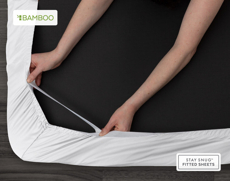 Vue du bas de notre Bamboo Cotton Fitted drap en blanc pour montrer deux mains tirant les élastiques Snug Fit qui maintiennent le coin en place sur un matelas.