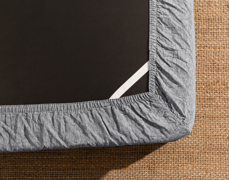 Le dessous d'un matelas équipé de notre Signature European Linen Fitted drap en Indigo Grey montre l'élastique Stay Snug qui le maintient en place.