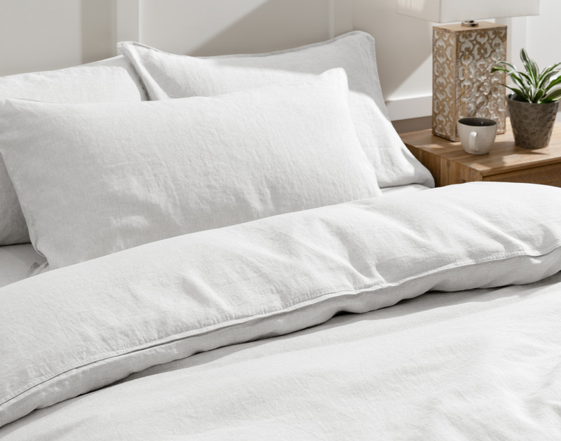 Angled view of our Signature European Linen Duvet Cover in White tidily made over a queen bed with a king-sized pillow at the top.