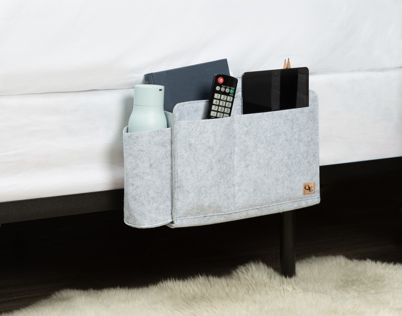 Side view of our Bedside Felt Pocket in Light Grey with living room essentials like a remote, tablet, and water bottle.