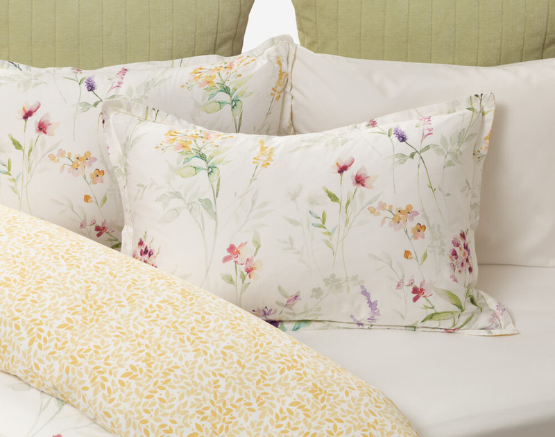 Notre Promise Floral Pillow Sham posé sur un lit blanc entrouvert.