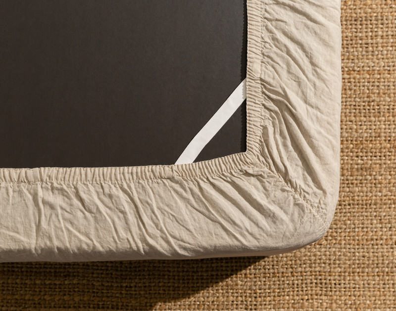 Le dessous d'un matelas équipé de notre Signature European Linen Fitted drap en Natural montre l'élastique Stay Snug qui le maintient en place.