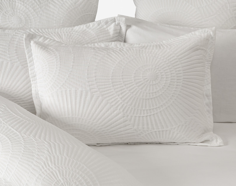 Our Boca White Pillow Sham sitting on a half-open white bed against other white pillows.