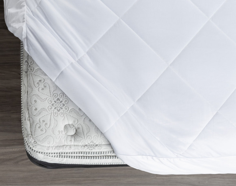 Our Cool Touch Mattress Pad rolled towards an open mattress corner to show its softness and flexibility.