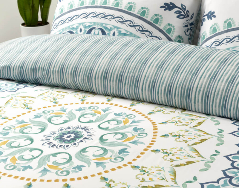 Angled view of our Chaya Duvet Cover's circular mandala pattern in green and yellow, with the folded reverse at the top.