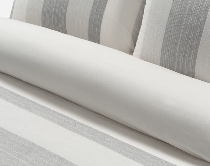 Close-up of rolled up top of our Oslo Duvet Cover to show its surface pattern and solid light grey cotton sateen reverse.