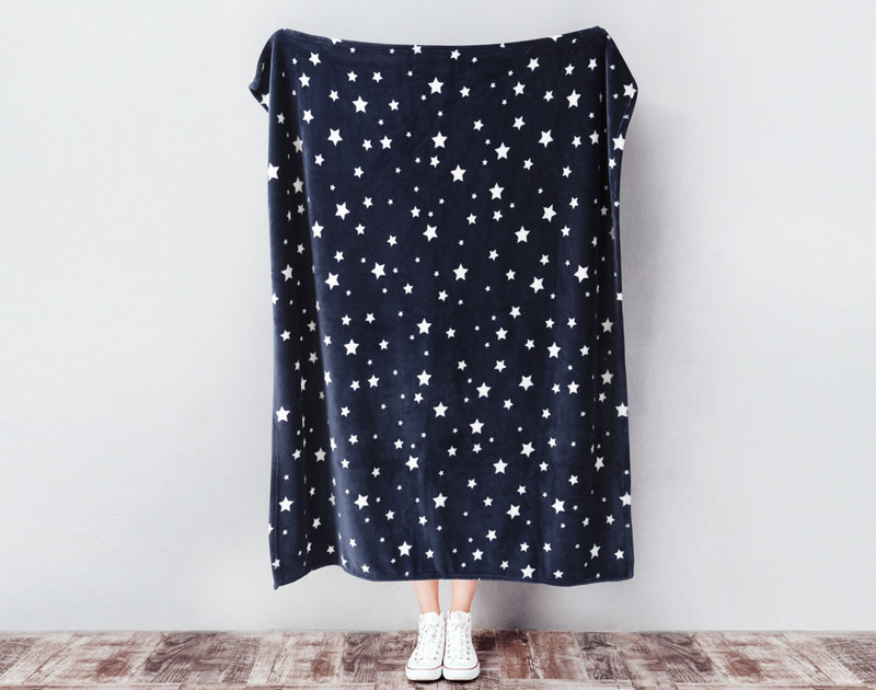 Our Kid's Fleece Velveteen Throw in Star being held against a wall with scattered white stars over a dark navy blue background.