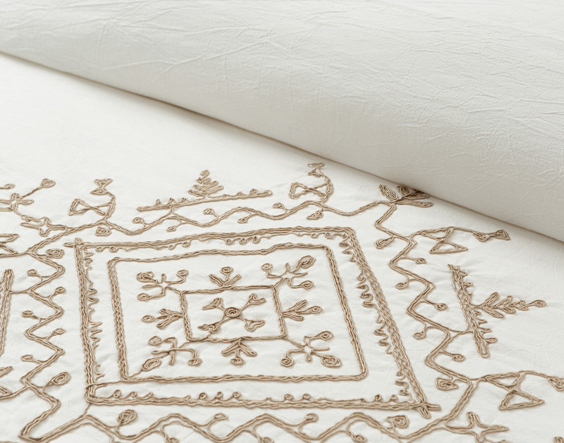 Close-up on the rolled top edge of our Mesa Duvet Cover to show its cotton crepe surface near its embroidered design.
