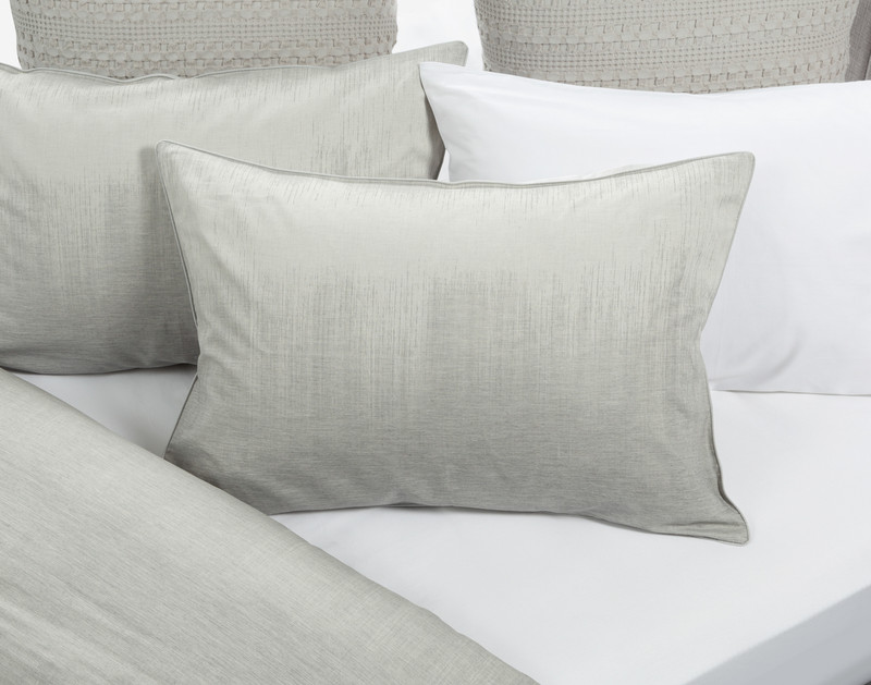 Our Benito Pillow Sham sitting against other coordinating pillows on a half-dressed white bed.