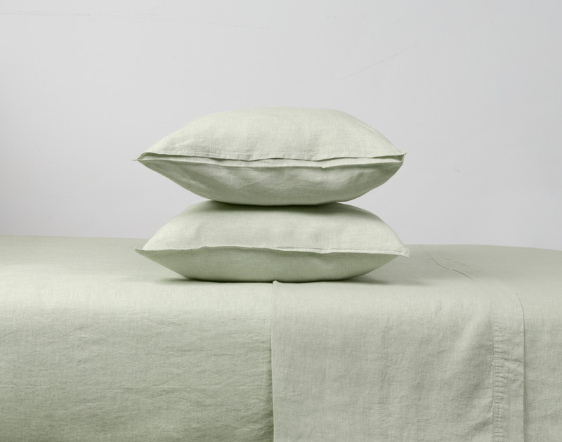 Taies d'oreiller en lin européen lavé vintage en vert sauge empilées verticalement sur un lit.