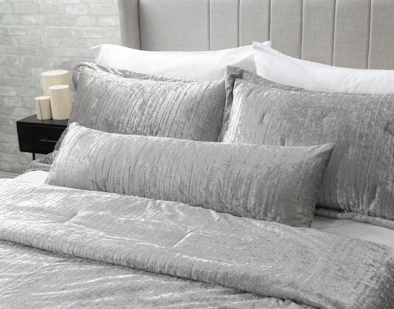 Angled view of our Avalon Lumbar Pillow in Silver sitting against coordinating pillows on a white bed.