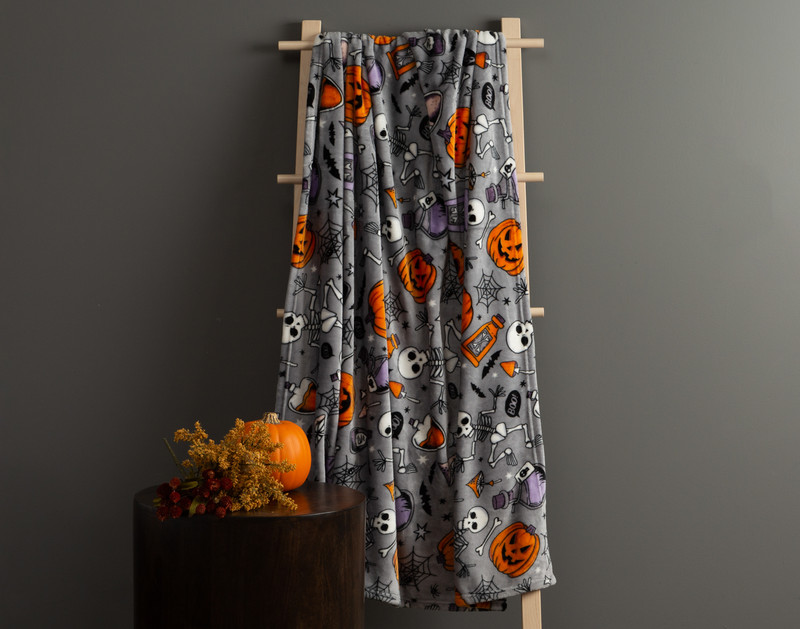 Our Halloween Fleece Throw in Magic Spell hanging from a ladder in a dark room, beside a small table with a pumpkin.