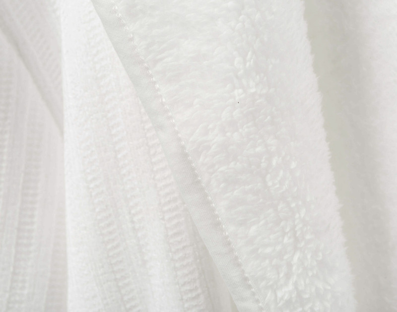 Gros plan sur le tissu de notre peignoir sherpa en chenille en blanc pour montrer à la fois sa doublure sherpa et sa surface chenille.