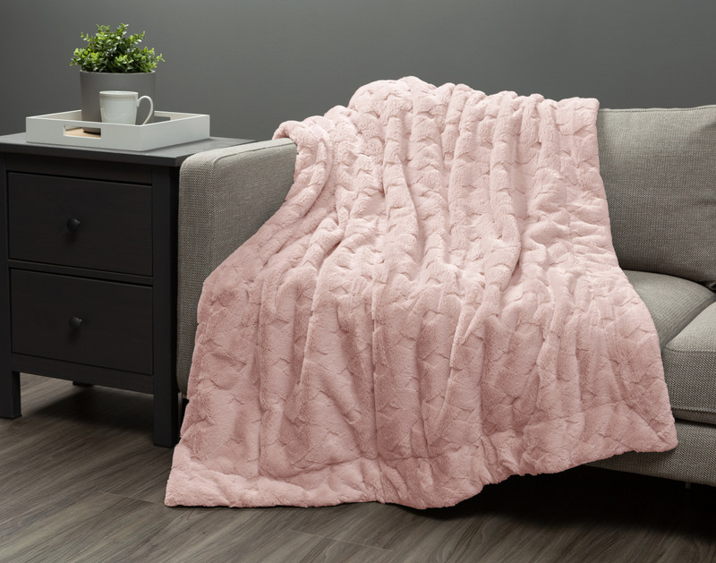 Our Etched Weave Throw in Blush draped over a grey couch in a dark living room.
