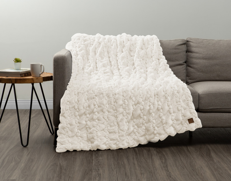 Our Rabbit Carved Faux Fur Throw in Snow draped over a couch in a grey bedroom.