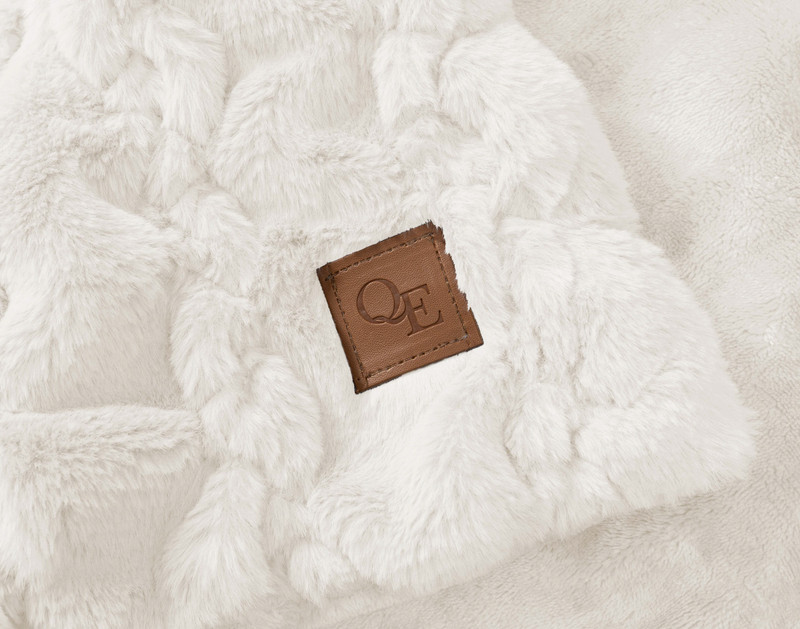 Close-up of the corner on our Rabbit Carved Faux Fur Throw in Snow featuring an embedded leather QE Home logo.