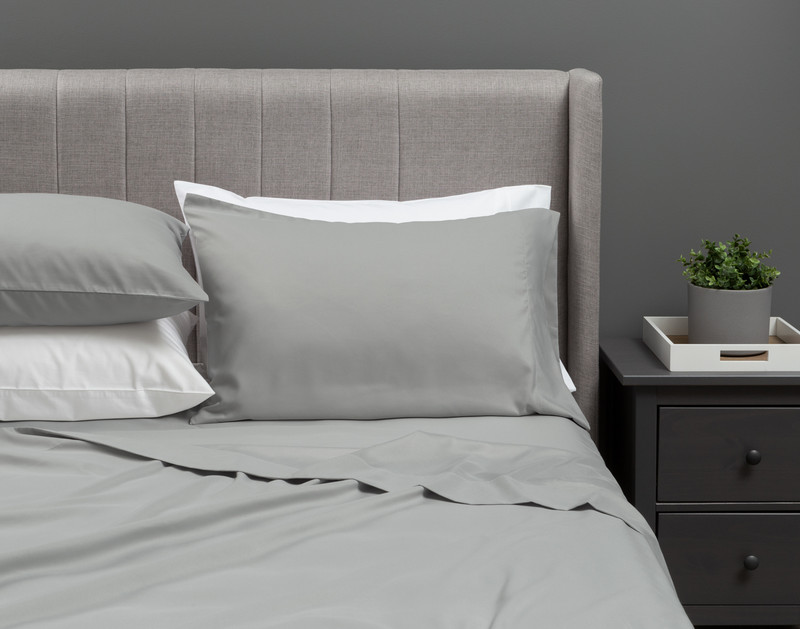 Our Recycled Microfiber Sheet Set in Smoke dressed over an undecorated bed in a neutral grey bedroom.