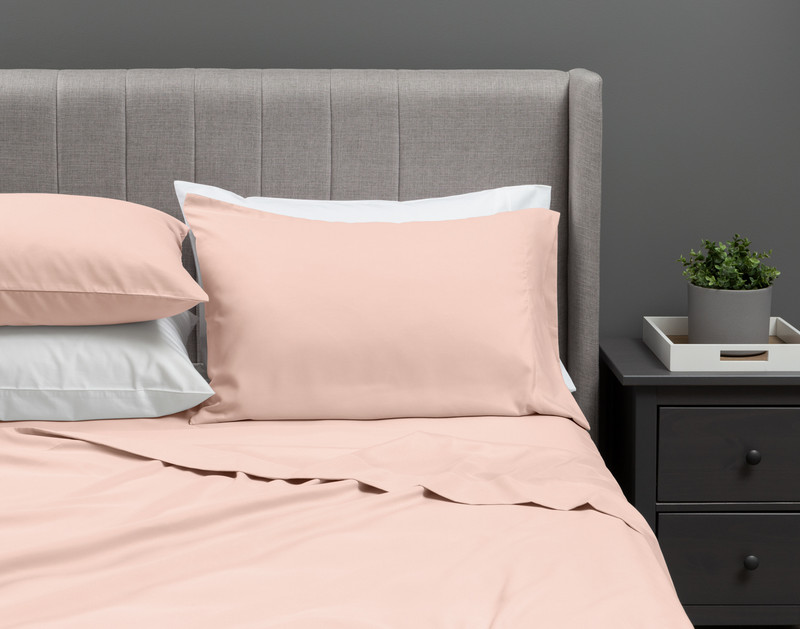 Our Recycled Microfiber Sheet Set in Blossom dressed over an undecorated bed in a neutral grey bedroom.