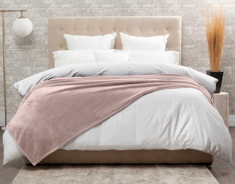 Vue de face de notre couverture Cashmere Touch polaire en Woodrose Pink drapée sur un lit blanc bien rangé.