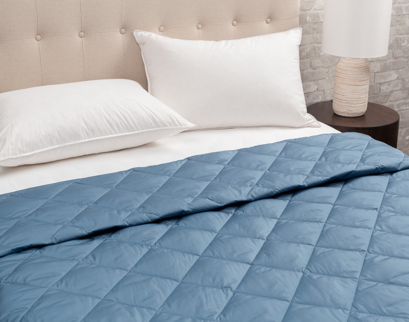 Vue en angle de notre couverture en duvet Packable en bleu nuit, format queen size, habillée sur un lit blanc pour montrer sa taille.