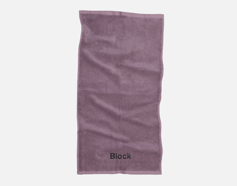 Notre serviette à main en coton modal Lilac Cendré repose sur un fond blanc uni avec le mot "Block" brodé dans notre police Block noire le long du bord inférieur.