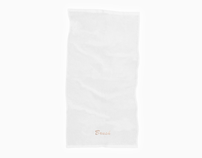 Notre serviette en coton modal blanc repose sur un fond blanc uni avec le mot "Brush" brodé dans notre police champagne Brush le long du bord inférieur.