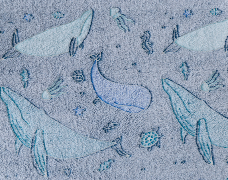 Close-up on our Whale Pod Glow in the Dark Fleece Throw to show its beluga whale design over an indigo background.