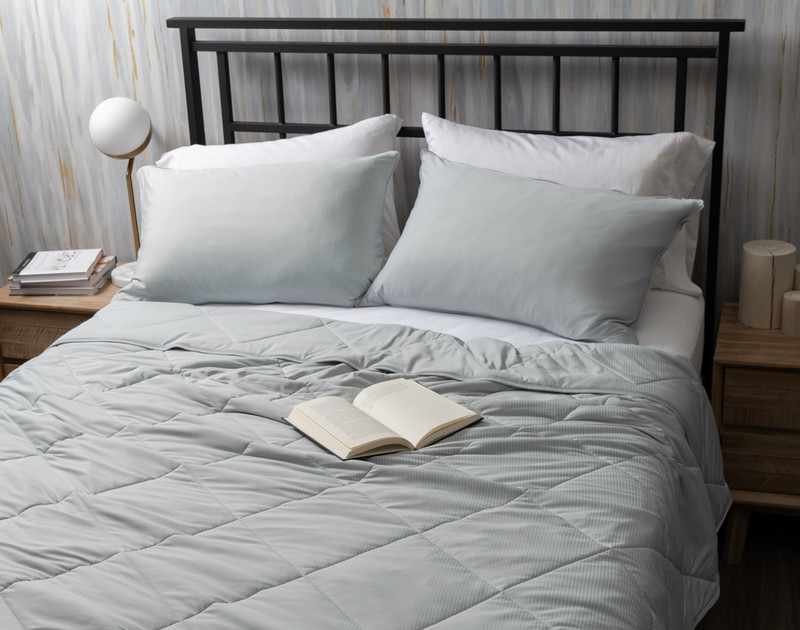 Top view of our Cool Touch Blanket in Grey Stripe spread over a queen bed with coordinating pillowcases and a book resting over it.