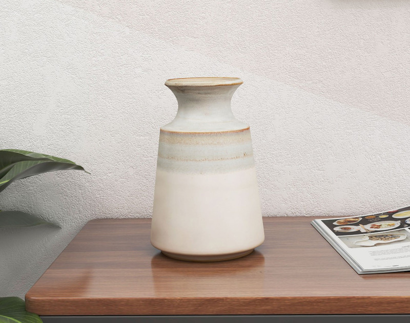 Vue de face de notre vase de table en céramique Nahla, posé sur une table d'appoint en bois bien rangée, contre un mur blanc crème.