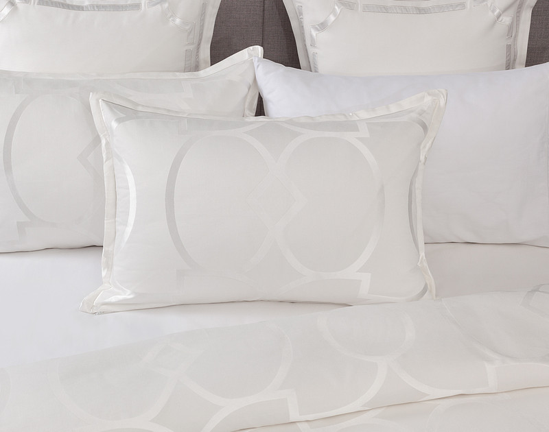 Notre oreiller Avenue Pillow Sham repose contre des oreillers coordonnés sur un lit blanc à moitié habillé.