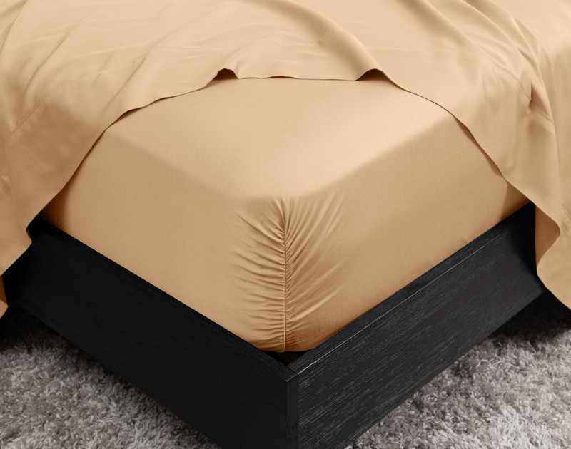 Close-up of the corner on our BeechBliss TENCEL™ Modal Fitted Sheet in Cashew snugly fit over a mattress with a flat sheet draped on top.