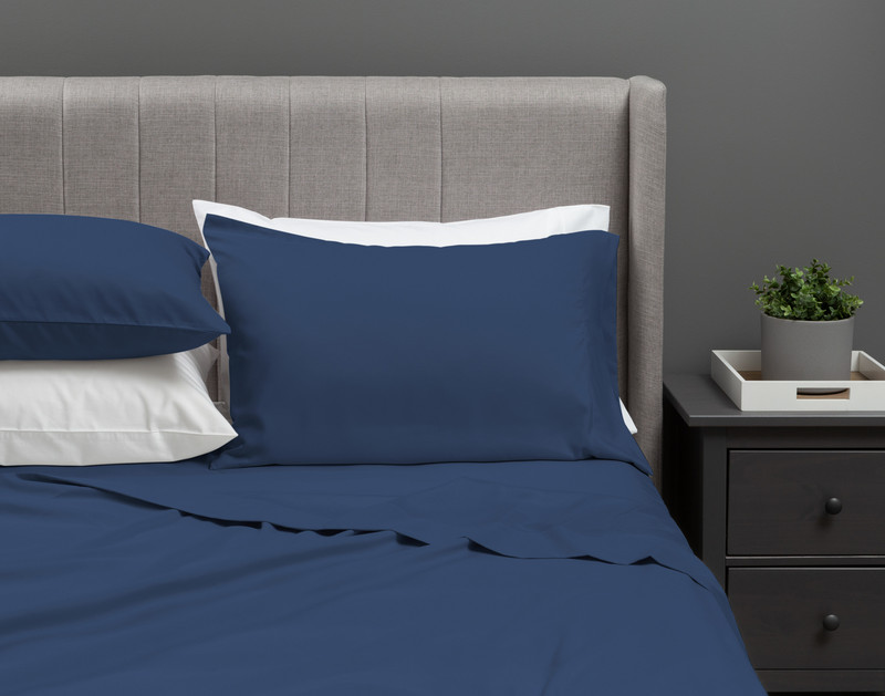 Our Recycled Microfiber Sheet Set in Denim dressed over an undecorated bed in a neutral grey bedroom.