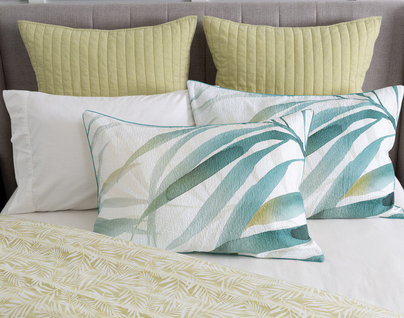 Our Bonita Pillow Sham resting on coordinating pillows over a white half-dressed bed.